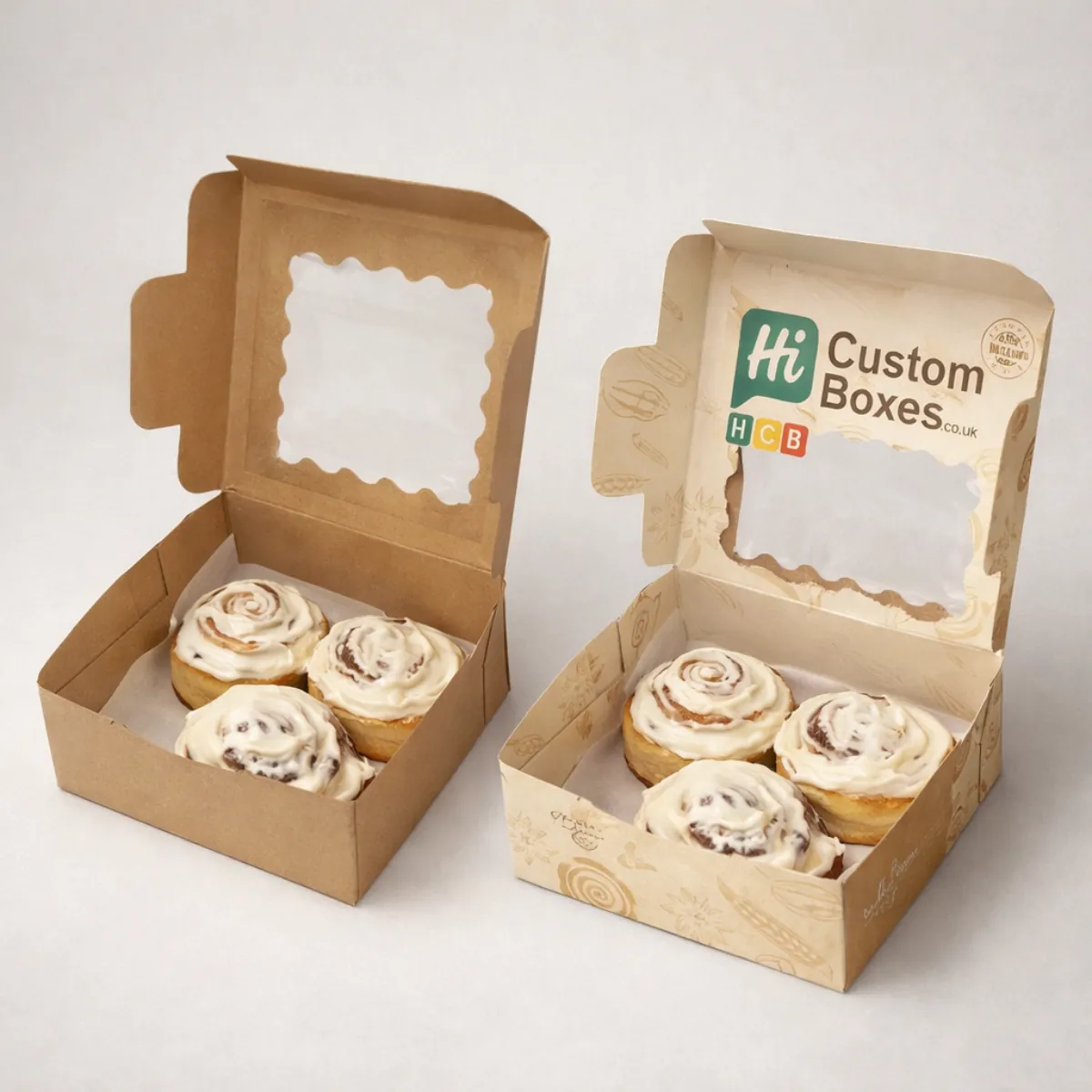 Two small square pastry boxes with scalloped window lids, displaying four generously frosted cinnamon rolls in each. class=